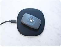Petivity Smart GPS and activity tracker for dogs resting on a black wireless charging pad on a white surface