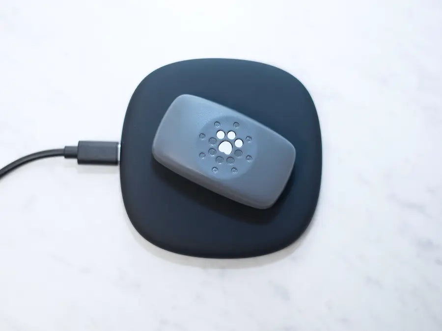 Petivity Smart GPS and activity tracker for dogs on a black wireless charging pad with a USB cable attached
